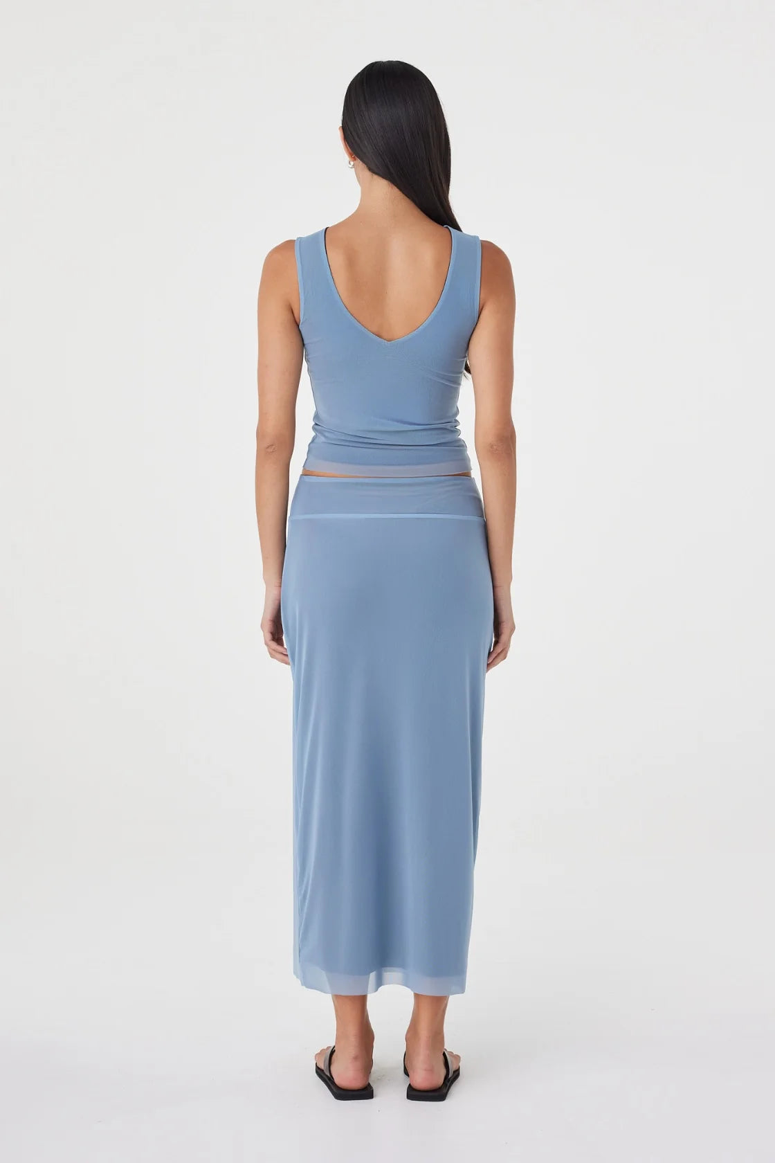 Back view of the pale blue reversible maxi skirt styled with a matching pale blue sleeveless top and black sandals against a clean white studio background.