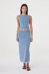 Full-length front view of the pale blue reversible maxi skirt styled with a matching pale blue sleeveless top and black sandals in a clean white studio.