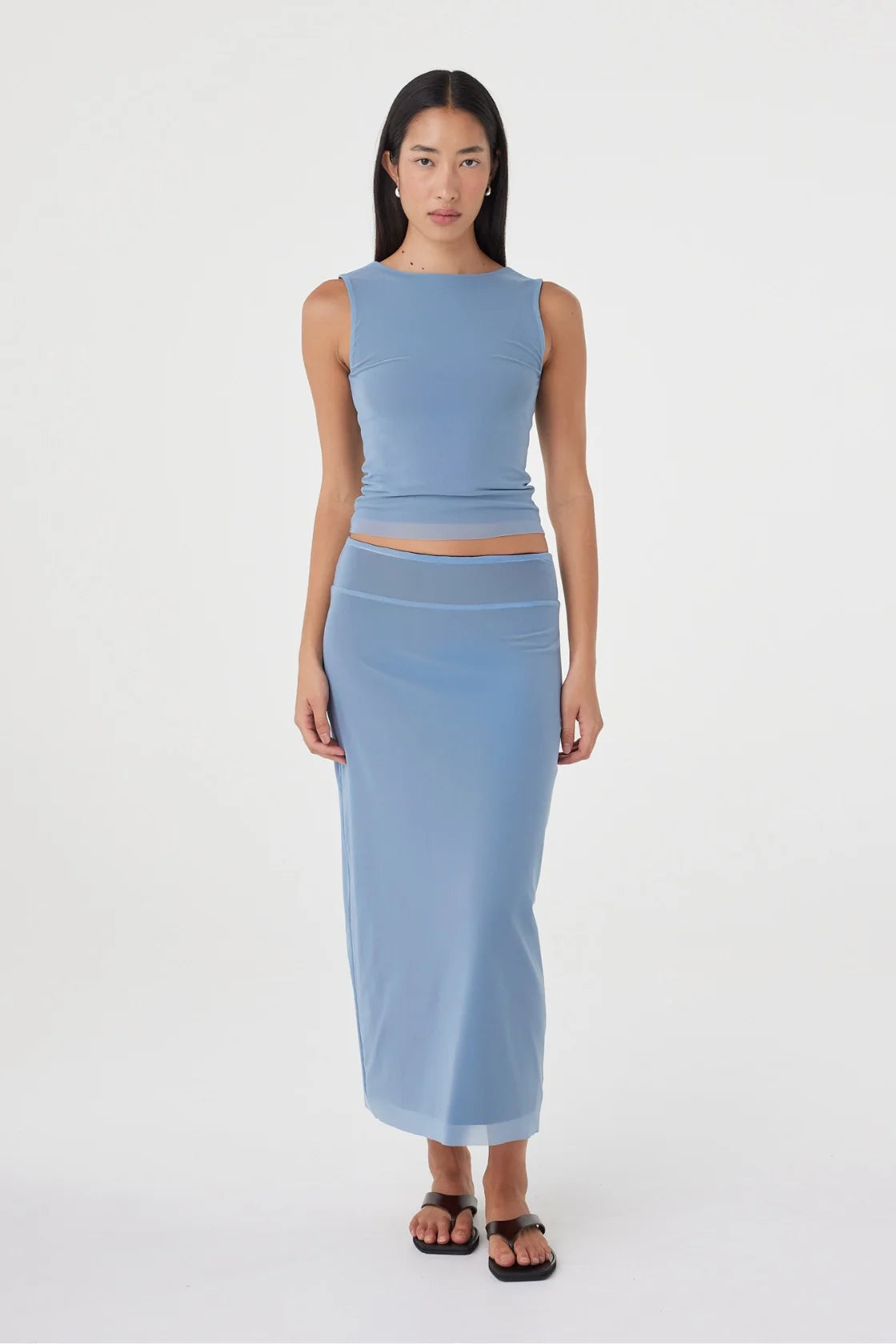 Full-length front view of the pale blue reversible maxi skirt styled with a matching pale blue sleeveless top and black sandals in a clean white studio.
