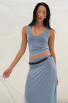Pale blue reversible maxi skirt styled with a matching pale blue sleeveless top and beaded belt in a relaxed pose against soft white curtains.