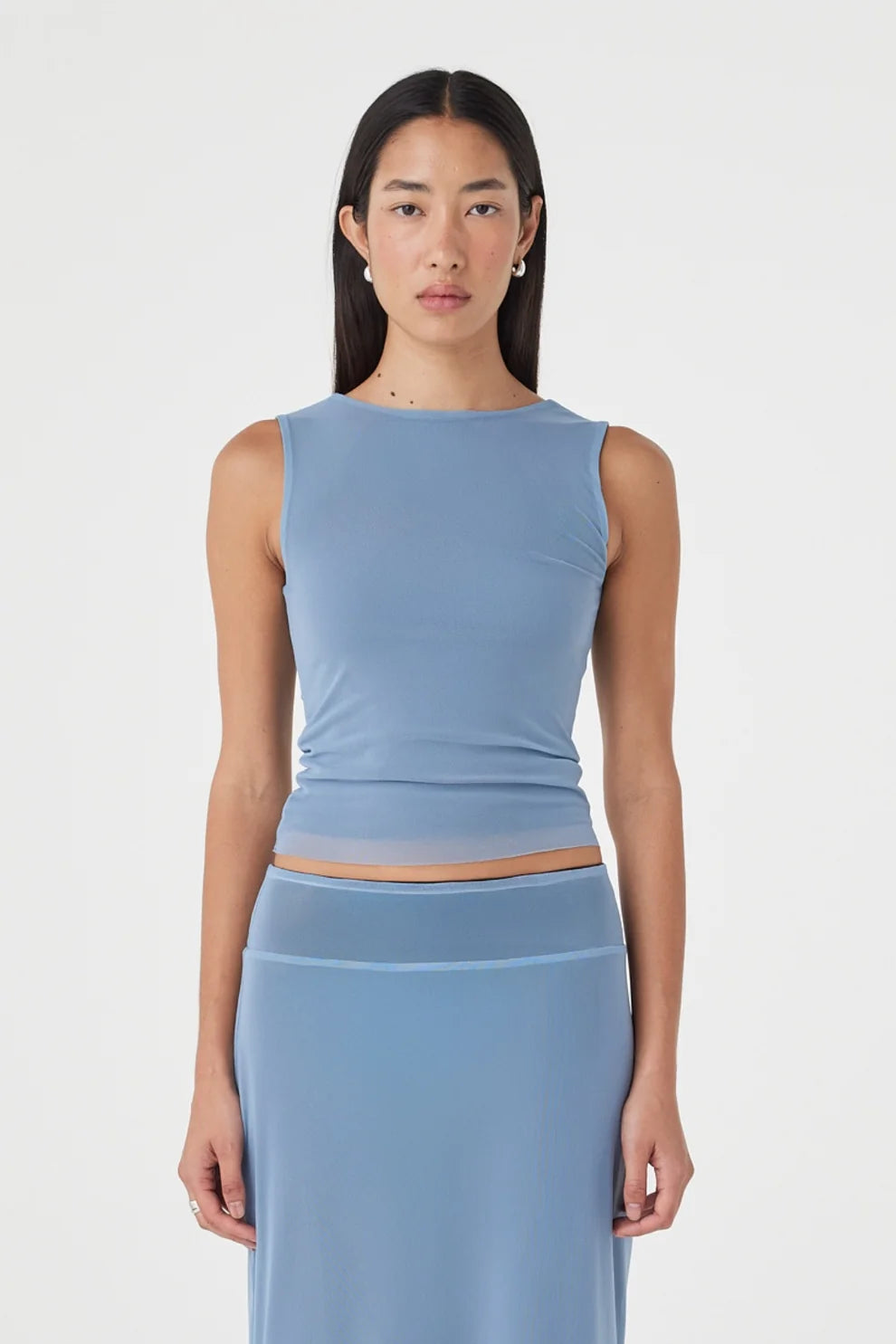 Close-up front view of the pale blue sleeveless reversible top with a high boat neckline and fitted silhouette, paired with the matching pale blue maxi skirt against a clean white studio background.