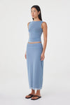 Three-quarter side view of the pale blue sleeveless fitted top paired with the matching pale blue maxi skirt and black sandals in a minimal white studio.