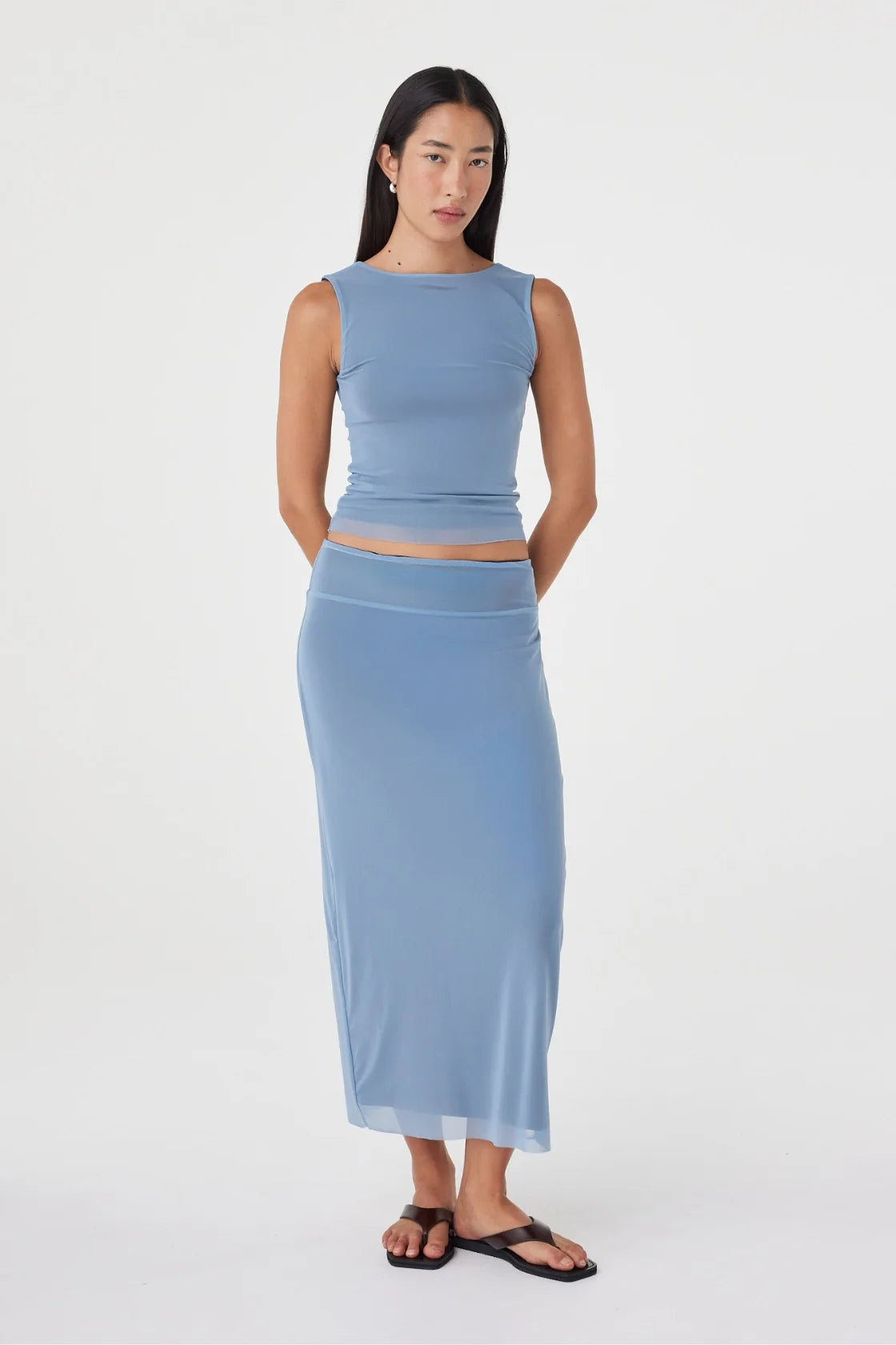 Full-length front view of the pale blue sleeveless top and matching maxi skirt, with the model standing with her hands behind her back in a clean white studio.