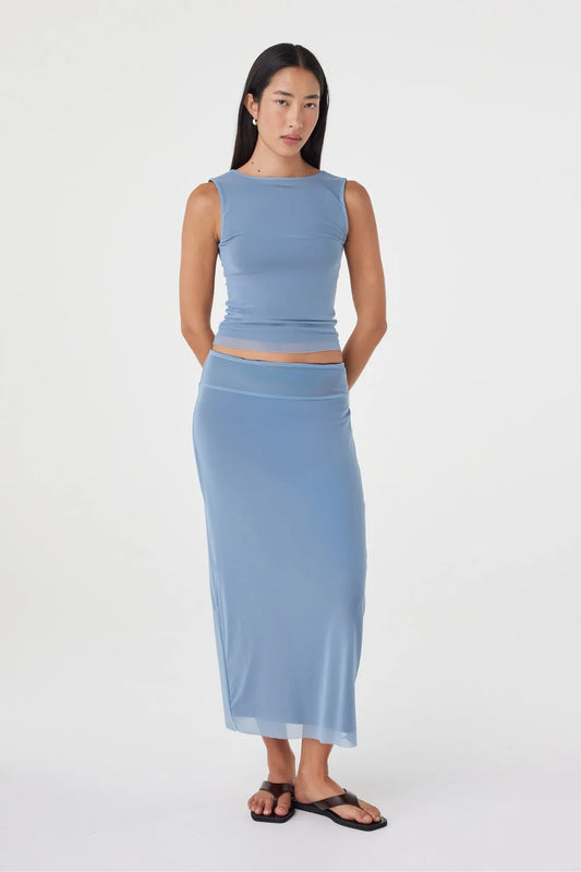 Full-length front view of the pale blue sleeveless top and matching maxi skirt, with the model standing with her hands behind her back in a clean white studio.