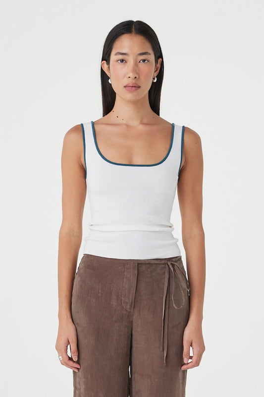Close-up front view of the cream fitted tank showing the teal contrast trim and scoop neckline, styled with brown wide-leg wrap pants against a clean white studio background.