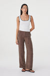 Front angled view of the cream fitted tank with teal contrast trim, styled with brown wide-leg wrap pants and black sandals in a relaxed pose against a white studio background.