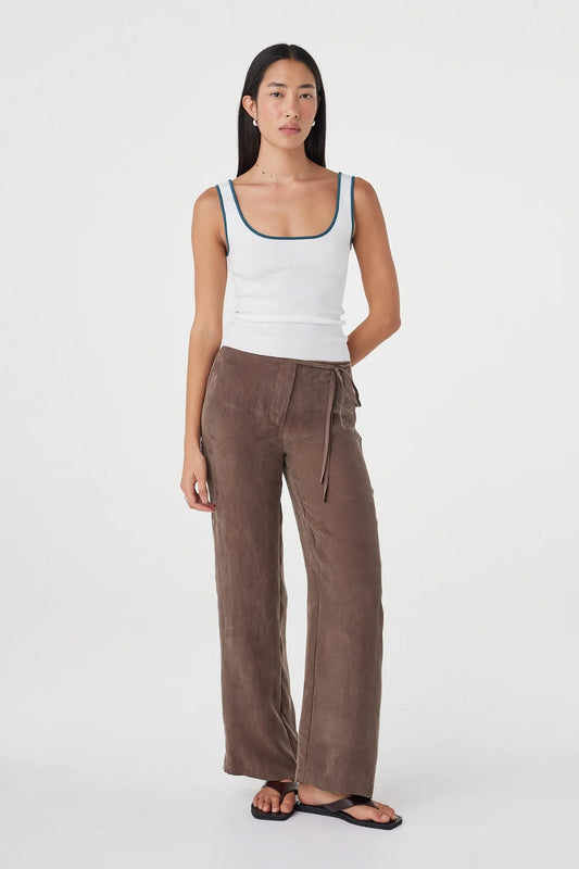 Front angled view of the cream fitted tank with teal contrast trim, styled with brown wide-leg wrap pants and black sandals in a relaxed pose against a white studio background.