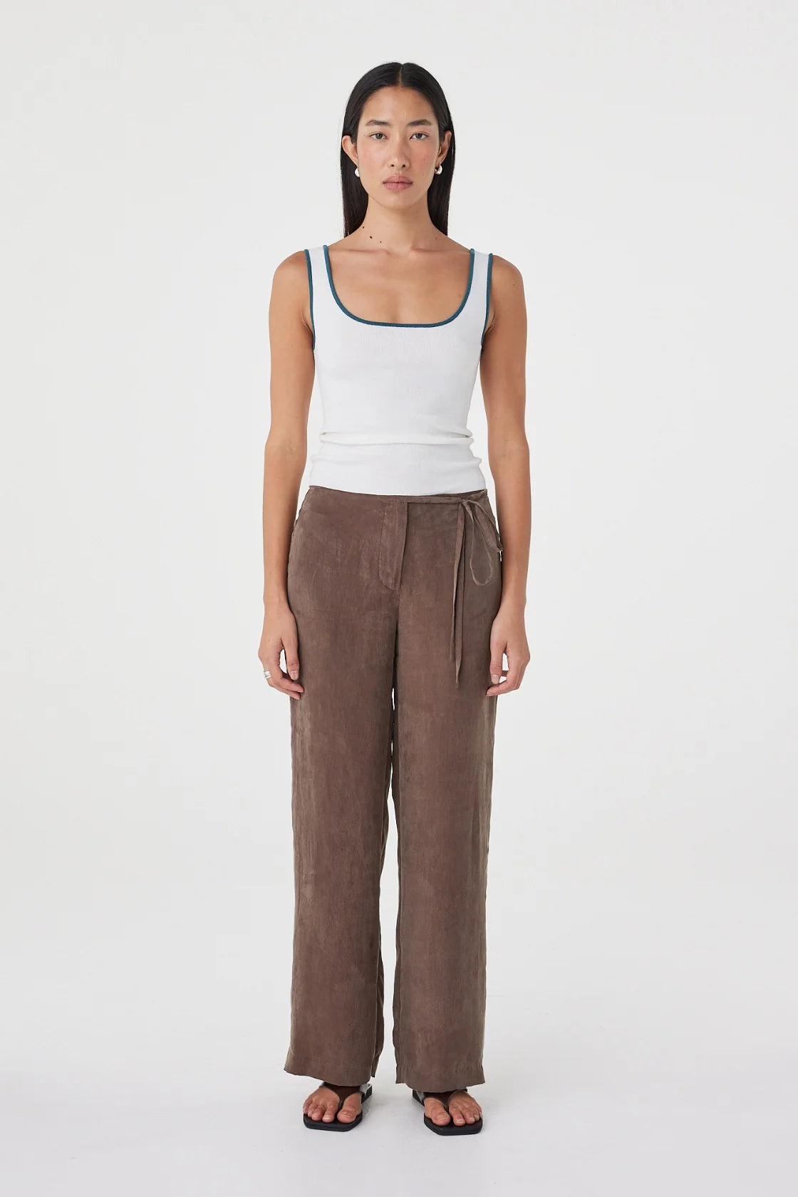 Full-length front view of the cream fitted tank with teal contrast trim, styled with brown wide-leg wrap pants and black sandals against a clean white studio background.