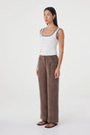 Three-quarter side view of the cream fitted tank with teal contrast trim, styled with brown wide-leg wrap pants and black sandals in a minimal white studio.