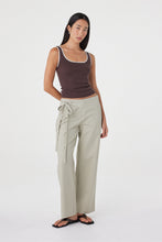 Model wearing the espresso fitted tank with cream wrap-style trousers, showing the contrast neckline and armhole trim, slim silhouette and hip-length finish in an angled front view.