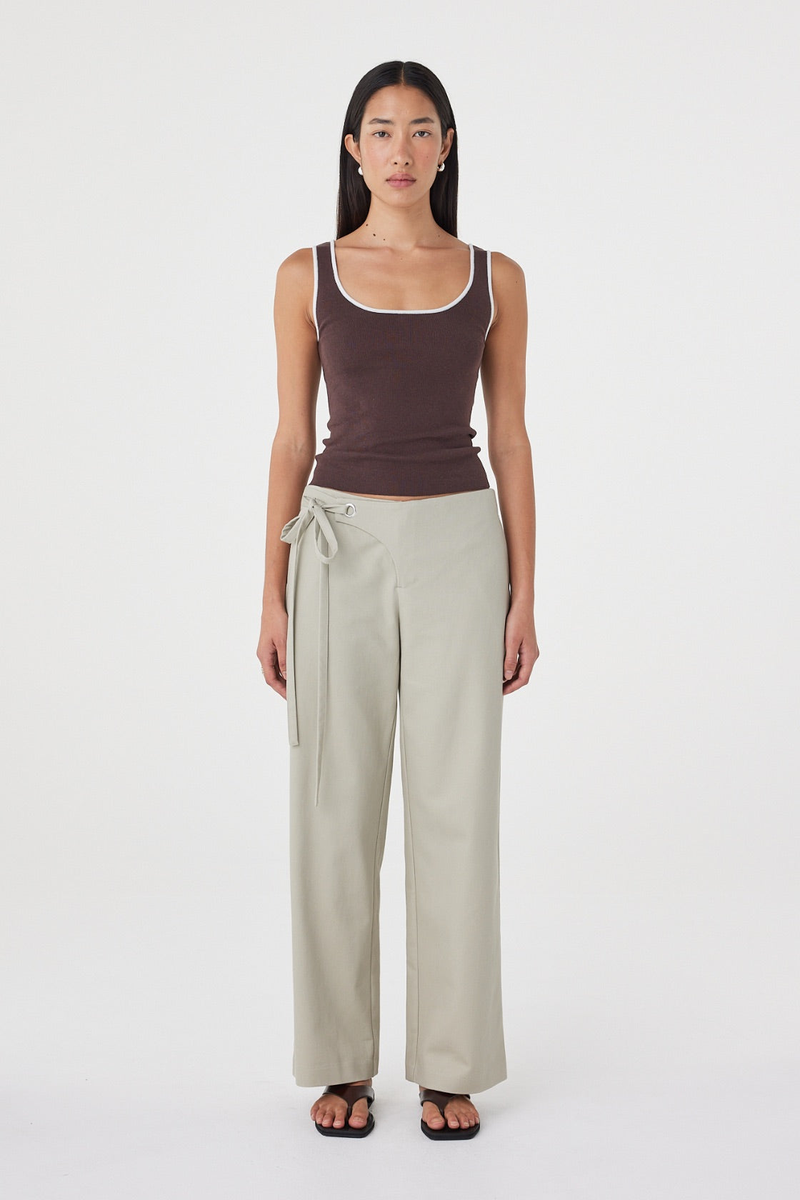 Model wearing the espresso tank with cream tailored trousers, showing the square scoop neckline, wide straps, contrast cream trim and close-fitting shape in a full-length front view.