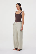 Model wearing the espresso tank with cream tailored trousers and black sandals, showing the square scoop neckline, contrast edging, fitted waist and streamlined silhouette in an angled side view.