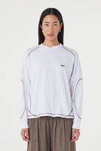 Close-up of the cream long-sleeve tee, showing the crew neckline, dropped shoulders, espresso overlock stitching, curved seam detailing and relaxed fit.