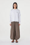 Model wearing the cream long-sleeve tee with brown check trousers, showing the crew neckline, long sleeves, espresso contrast stitching and relaxed off-body silhouette in a full-length front view.