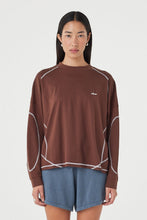 Close-up of the espresso long-sleeve tee, showing the crew neckline, dropped shoulders, contrast cream overlock stitching, curved seam detailing and relaxed fit.