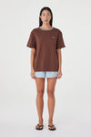 Full-length front view of the espresso oversized tee with cream contrast trim, styled with pale blue shorts and black sandals against a clean white studio background.
