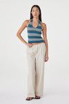 Front angled view of the teal striped halter top styled with cream wide-leg pants and black sandals in a white studio.