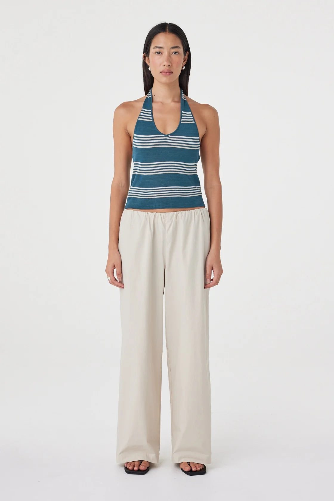 Full-length front view of the teal striped halter top paired with cream wide-leg pants and black sandals against a clean white studio background.