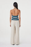 Back view of the teal striped halter top showing the open back, styled with cream wide-leg pants in a clean white studio.