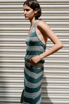 Side view of the teal striped halter top styled with a matching striped skirt against a metal shutter background.