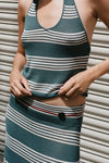 Close-up front view of the teal striped halter top styled with a matching striped skirt against a metal shutter background.