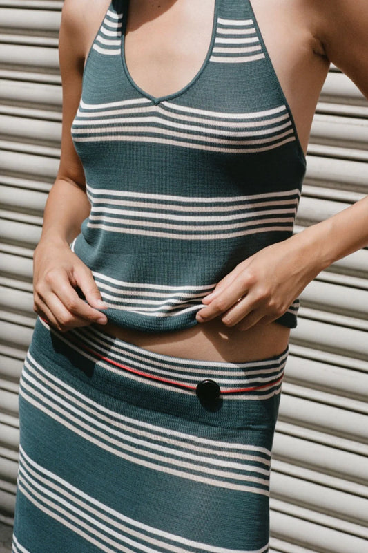 Close-up front view of the teal striped halter top styled with a matching striped skirt against a metal shutter background.