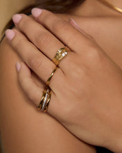Close-up of two hands styled with the Indigo Gold Ring and several delicate gold rings, showing the layered band design from above.