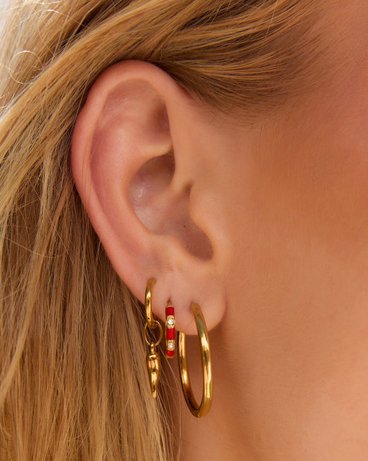 Arms Of Eve Papaya Enamel Huggies Cherry styled in a layered gold earring stack.