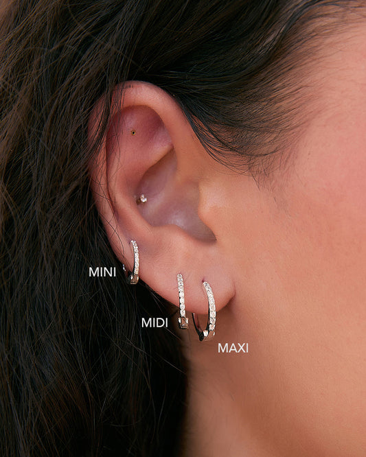 Close-up of an ear wearing three hoop earrings labeled 'MINI', 'MIDI', and 'MAXI'.