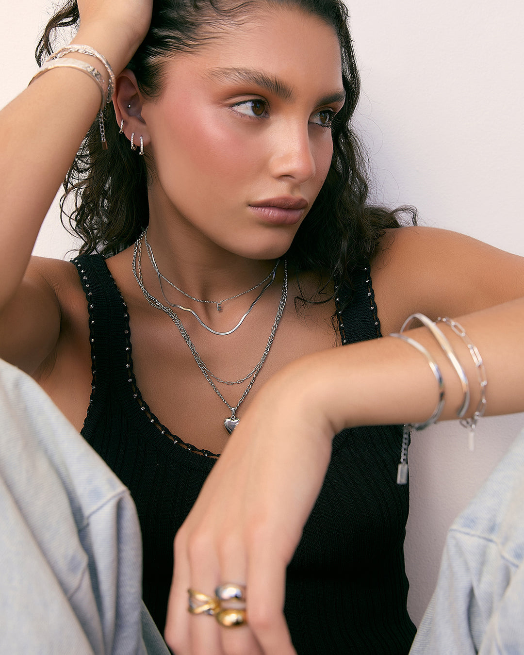 Woman wearing multiple necklaces and bracelets on a plain background
