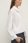 Side view of a white cropped shirt showing the pointed collar, button front and long sleeve construction.