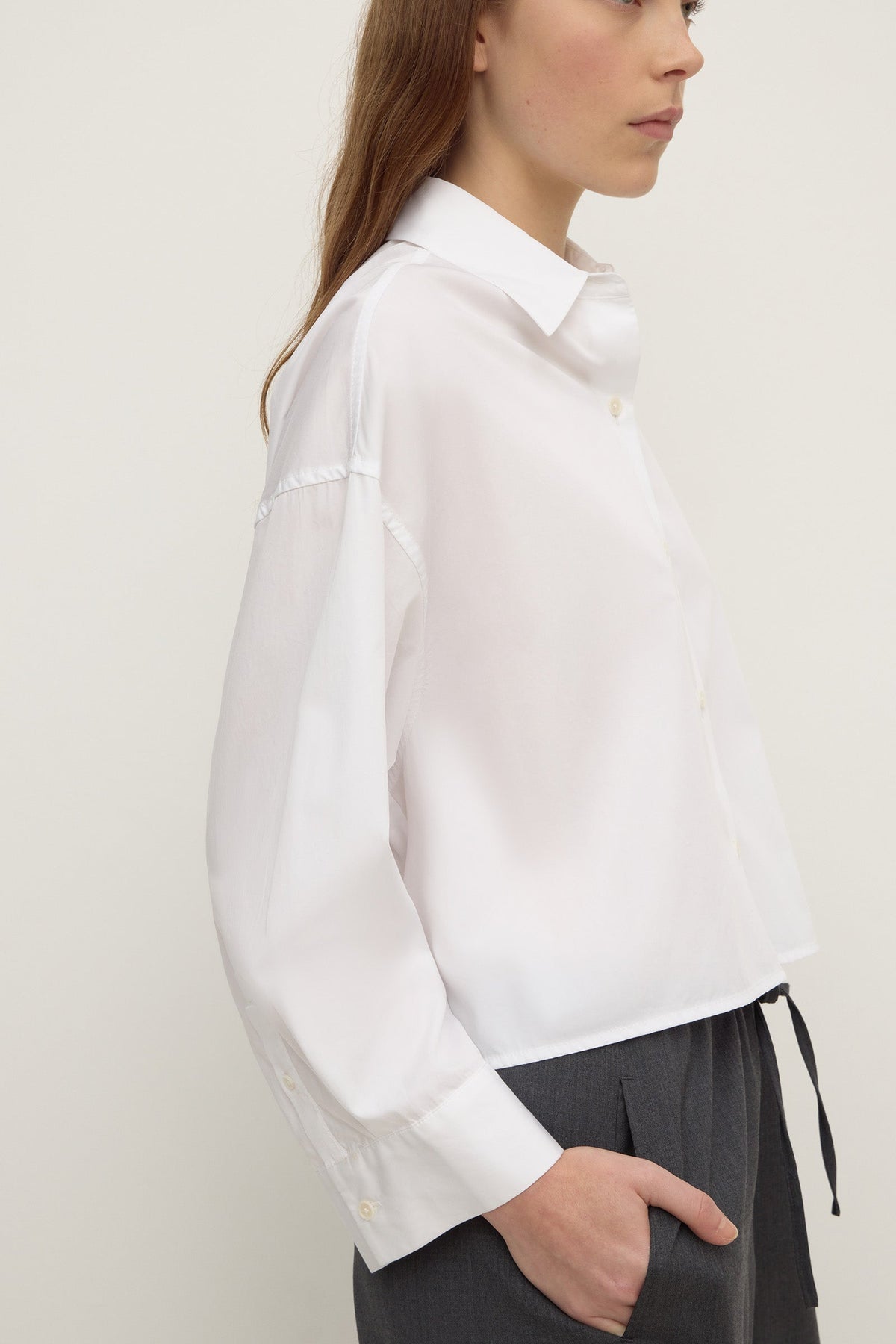 Side view of a white cropped shirt showing the pointed collar, button front and long sleeve construction.