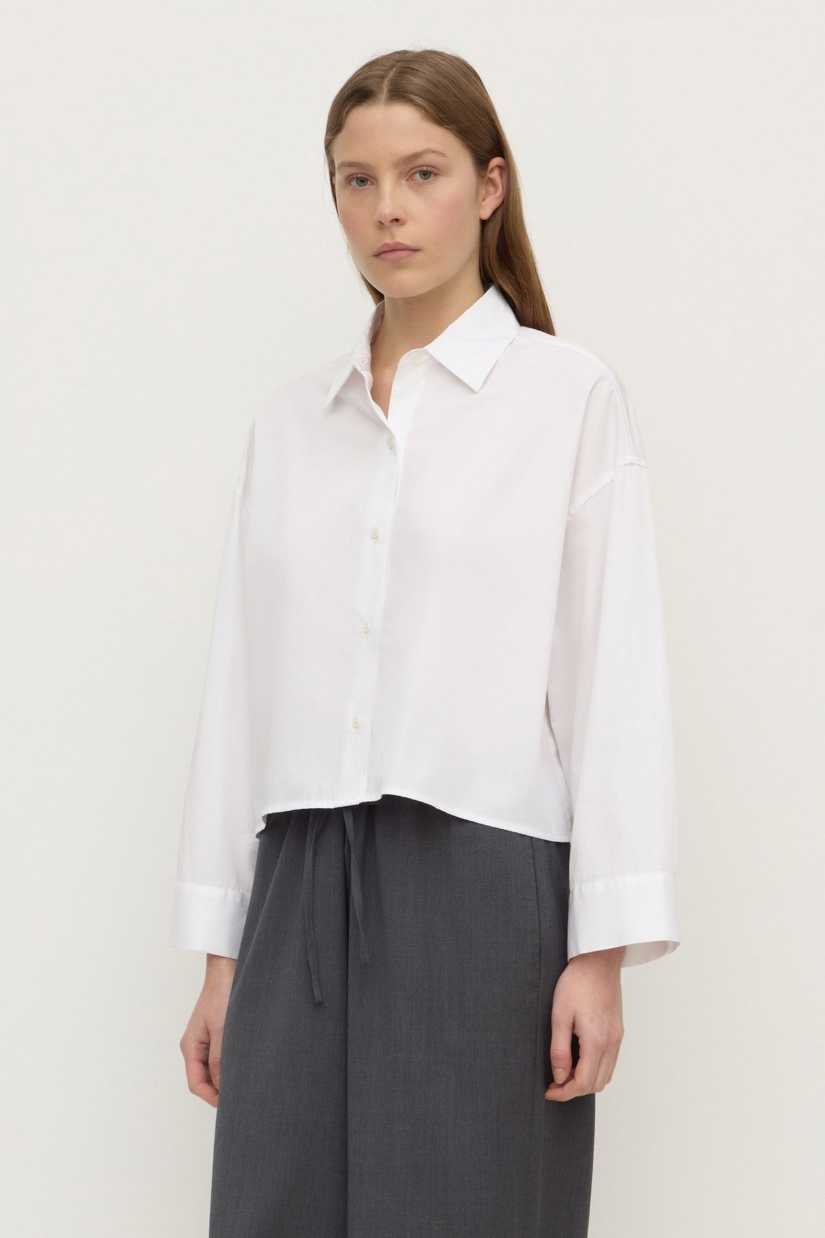 Three-quarter view showing the white shirt's cropped hem, button front and long sleeves.
