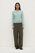 Woman wearing a light blue cardigan and green pants on a white background
