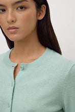Woman wearing a light green cardigan against a plain background