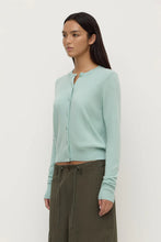 Woman wearing a light blue cardigan and green pants on a white background