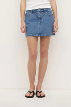 Model wearing the dark stone denim mini skirt with a white tank and black sandals, showing the straight hem, fitted waist and structured denim silhouette, front view
