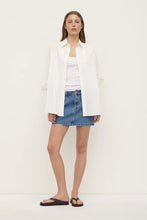 Model wearing the dark stone denim mini skirt with a white tank, oversized white shirt and black sandals, showing the mid-rise fit and mini length, styled front view
