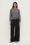A model wearing black wide-leg pants with an elasticated waistband, relaxed silhouette and full-length hems, shown from the front.