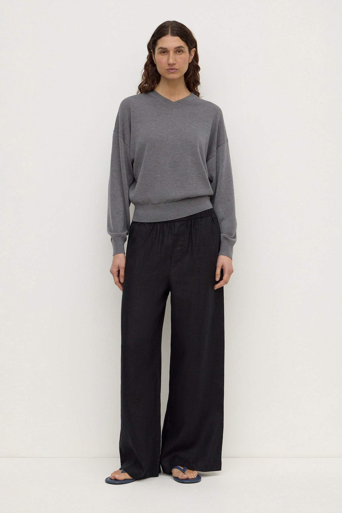 A model wearing black wide-leg pants with an elasticated waistband, relaxed silhouette and full-length hems, shown from the front.