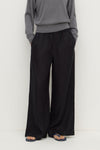 Close-up front view of black wide-leg pants showing the gathered elasticated waistband, side pockets and flowing leg shape.