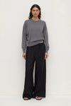 A model wearing black wide-leg pants with a relaxed silhouette and full-length hems, shown from the front with hands at the sides.