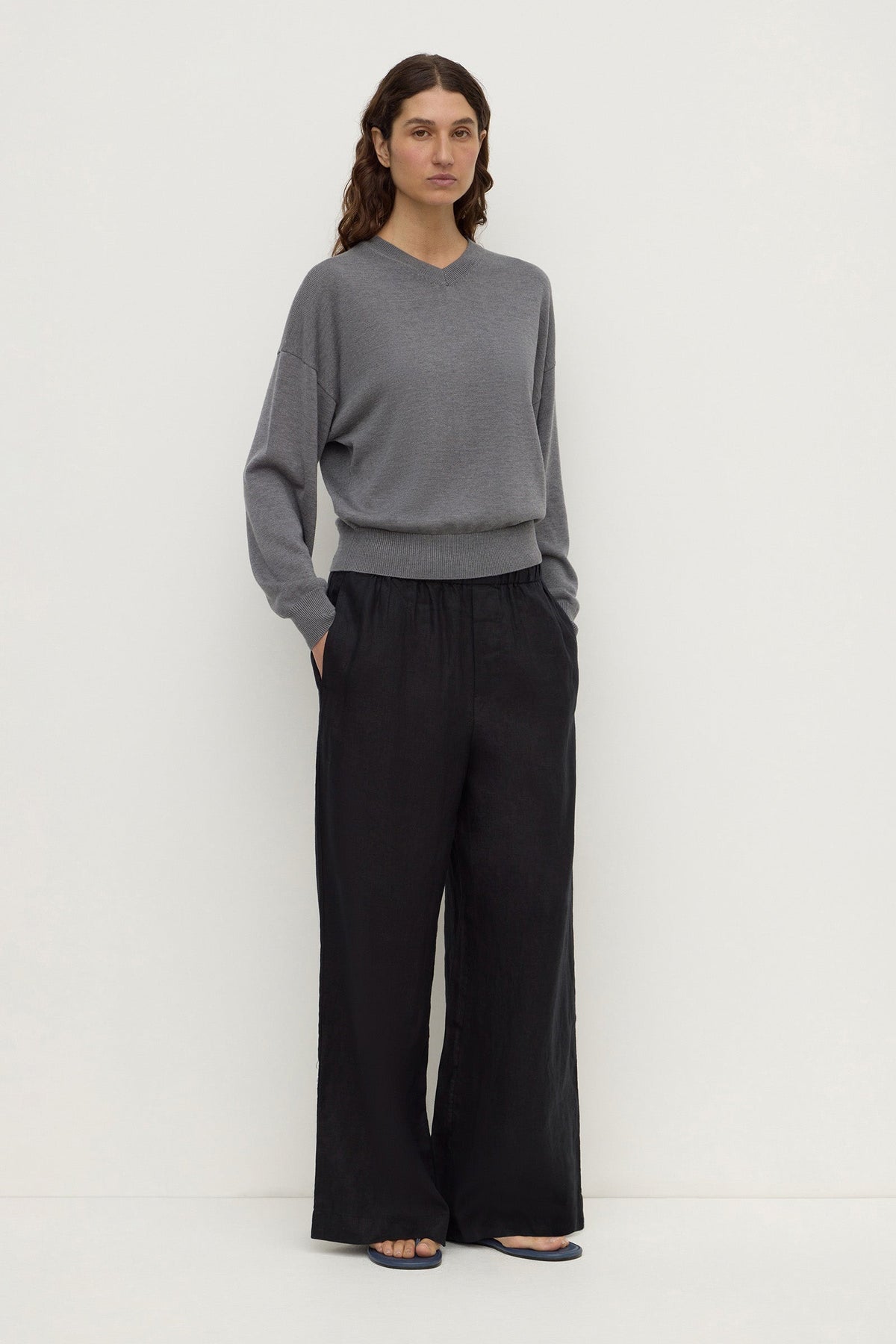 A model wearing black wide-leg pants from a three-quarter view, showing the wide legs, elasticated waistband and side pockets.
