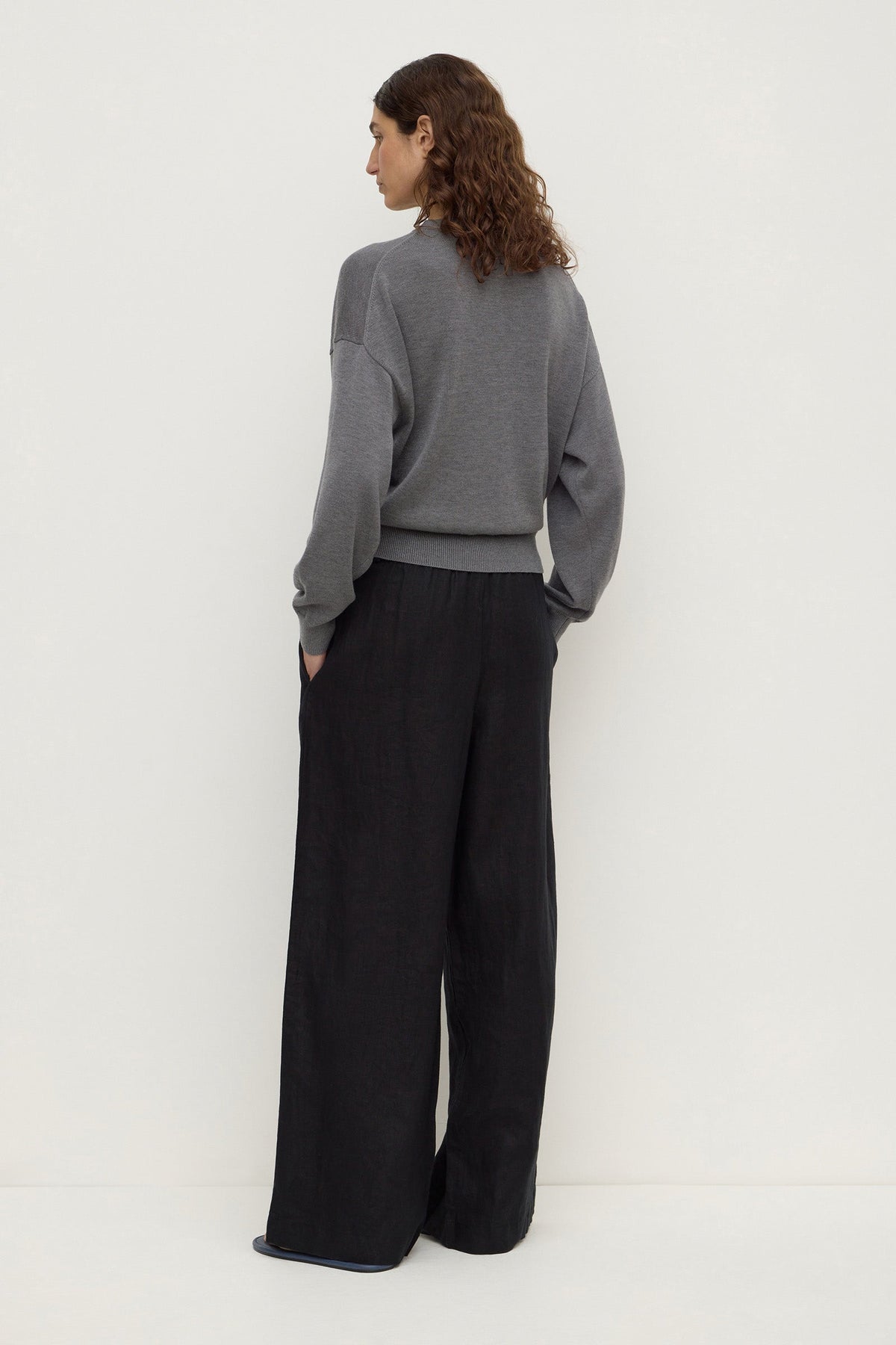 Back view of a model wearing black wide-leg pants, showing the relaxed shape, elasticated waistband and full-length legs.