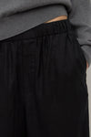 Close-up view of black pants showing the gathered elasticated waistband, internal waist construction and side pocket opening.