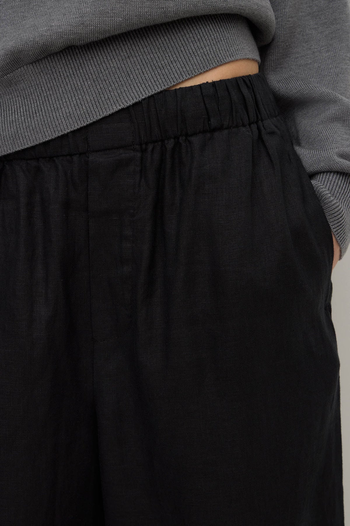 Close-up view of black pants showing the gathered elasticated waistband, internal waist construction and side pocket opening.