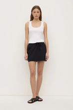 Model wearing the black poplin mini skirt with a fitted white tank and black sandals, showing the mid-rise waist, drawstring detail and relaxed mini-length silhouette, front view
