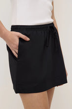 Close-up of the black poplin mini skirt, showing the elasticated drawstring waistband, side seam pocket and crisp cotton fabric, front detail view
