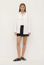 Model wearing the black mini skirt with a white tank, oversized white shirt and black sandals, showing the relaxed mini silhouette in a layered outfit, full-length front view
