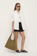 Model wearing the black mini skirt with an oversized white shirt, black sandals and an olive tote bag, showing the mid-rise fit and mini-length hem, styled front view